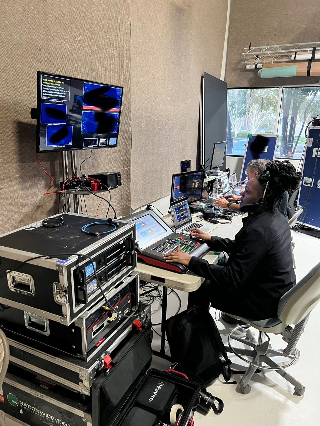 Operator using a video switching console beside equipment racks and multiview monitors.